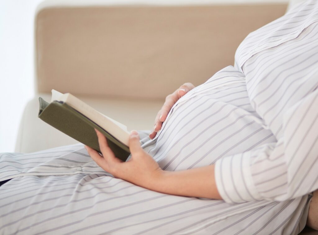 Kobieta w ciąży czyta porady dla kobiet w ciąży na kanapie