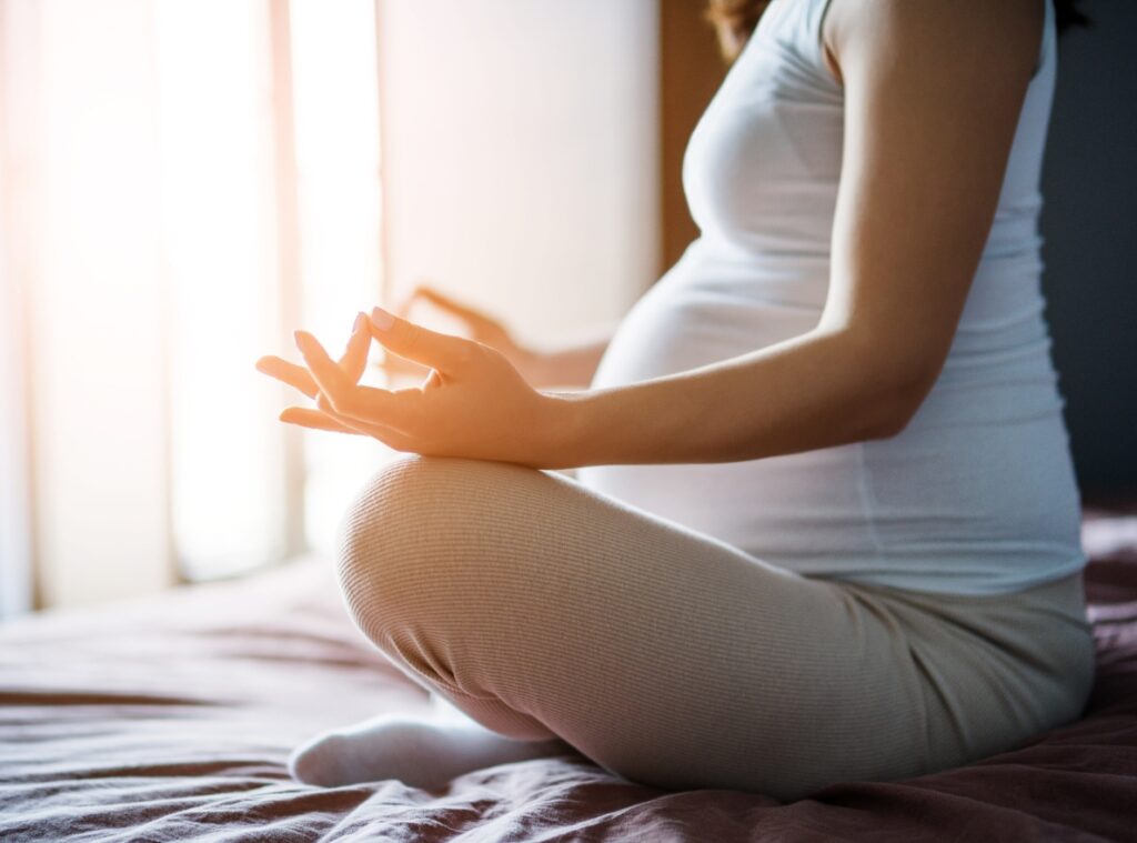 Przyszła mama w ciąży siedzi zrelaksowana na łóżku i medytuje